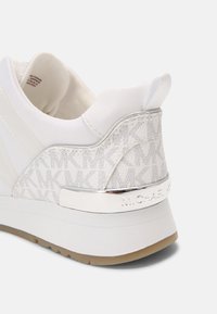 Sneaker bianco con tomaia testurizzata e con pattern, arricchita da dettagli metallici e una suola in gomma solida. Il marchio è visibile sul tallone.