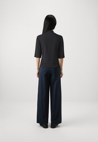 Top nero con maniche corte, abbinato a pantaloni a palazzo blu scuro dalla vestibilità ampia. Texture lisce, design minimal e colori solidi senza motivi.