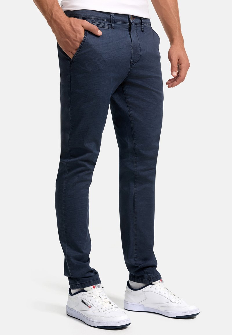 Marineblaue schmal geschnittene Chinos aus glattem Baumwollstoff, mit Seitentaschen und einem Reißverschluss, kombiniert mit weißen Sportschuhen.