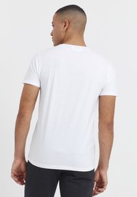 T-shirt en coton blanc à manches courtes, col rond et texture lisse, vu de dos. Les détails incluent une étiquette de marque discrète au niveau de l'encolure.