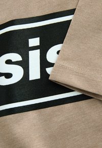Beige Baumwollstoff mit einem schwarz-weißen Druckdesign. Der Text "sis" ist auffällig und von einem rechteckigen schwarzen Rahmen umgeben.