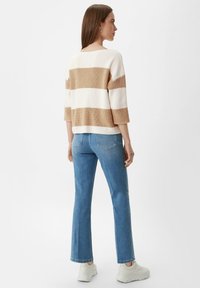 Beżowy i biały sweter w paski z rękawami o długości trzech czwartych, w połączeniu z jasnoniebieskimi dzwonami i białymi trampkami.