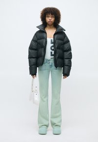 Doudoune noire, bodysuit graphique blanc, jeans évasés bleu clair, sabots menthe et sac à main blanc. Textures lisses et couleurs vives.