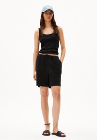 Black ribbed tank top and matching shorts with pockets, made of textured fabric. Pairing with dark slide sandals and a light blue cap.