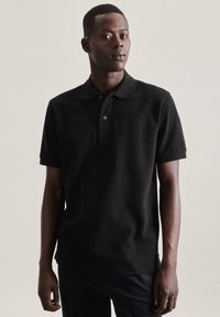 Polo nero realizzato in cotone con colletto classico, maniche corte e pattina con due bottoni. Texture morbida con una forma aderente.