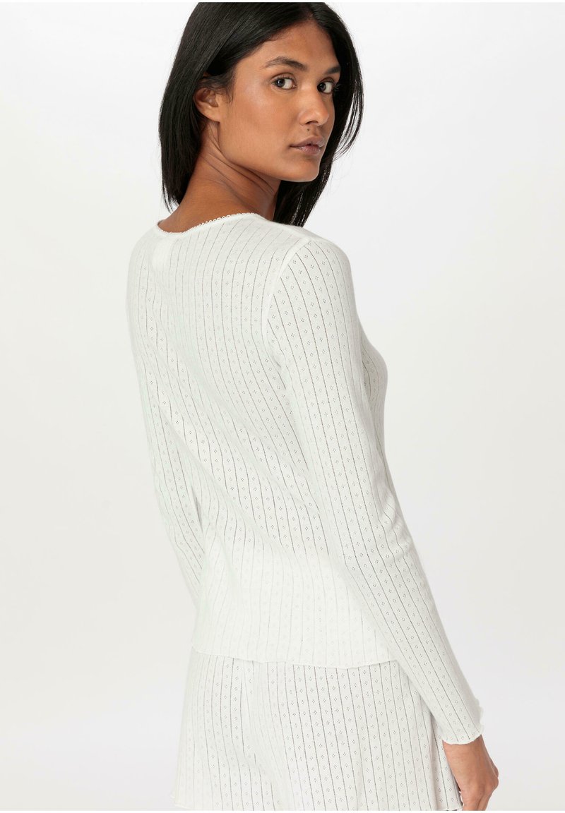 Weißes, geripptes Langarmoberteil mit einem gewellten Ausschnitt und strukturiertem Muster. Figurbetontes Design, weiches Material und eine leicht strukturierte Silhouette.