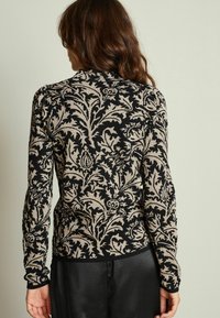 Maglione a maglia con motivo floreale nero e beige, a maniche lunghe, caratterizzato da dettagli intricati e una silhouette aderente. Tessuto morbido.