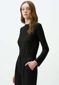Schwarzes Langarmshirt mit Rippstruktur und hohem Kragen, kombiniert mit maßgeschneiderten schwarzen Hosen mit Seitentaschen. Einfaches und elegantes Design.