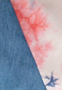 Bavlněná látka v modré a bílé barvě s červeným tie-dye vzorem. Materiál má měkkou strukturu a mírně texturovaný povrch.