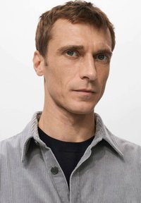 Camisa de pana gris con un cuello estructurado, detalle de botones y superficie texturizada, superpuesta sobre una camisa negra con escote redondo.