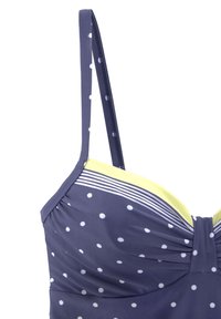 Námorníckom modrý bikiny top s bielymi bodkami, zhrnutou tkaninou, žltým kontrastným lemovaním a tenkými nastaviteľnými ramienkami so pruhovaným detailom.