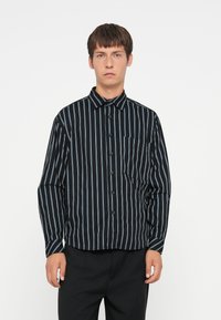 Zwarte overhemd met verticale blauwe strepen, borstzak, puntkraag en lange mouwen. Soepele stof met een casual pasvorm.