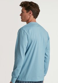 Lichtblauw shirt met lange mouwen en een ronde halslijn, met aansluitende manchetten. Gemaakt van zachte stof, met een gladde textuur en een relaxte pasvorm.