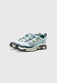 Chaussures de trail running avec une tige en maille respirante de couleur blanche et bleu sarcelle. Elles disposent d'une semelle rembourrée, d'un bout arrondi et d'une semelle extérieure texturée noire.