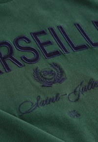 Grüner Sweatshirt mit marineblauem gesticktem Text "MARSEILLE" und "Saint-Julien", verziert mit einem dekorativen Lorbeerdesign und Gründungsdatum.