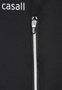 Černá atletická bunda na zip s texturovanou látkou. Má bílý zip a logo. Detailní záběr ukazuje detaily zipu a šití.