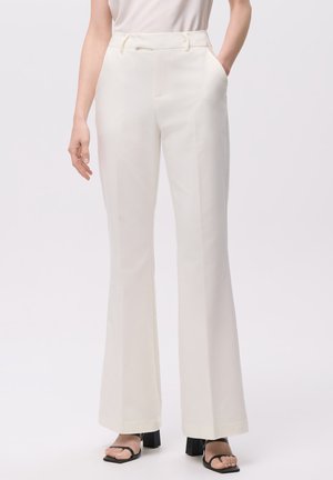 Pantalones blancos, ajustados y de cintura alta, con una textura suave y piernas acampanadas; cuentan con bolsillos laterales y pasadores para cinturón. Combinados con sandalias negras.