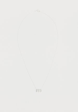 Collier délicat en chaîne argentée avec un petit pendentif en lettre minuscule "m" suspendu au centre sur un fond blanc uni.