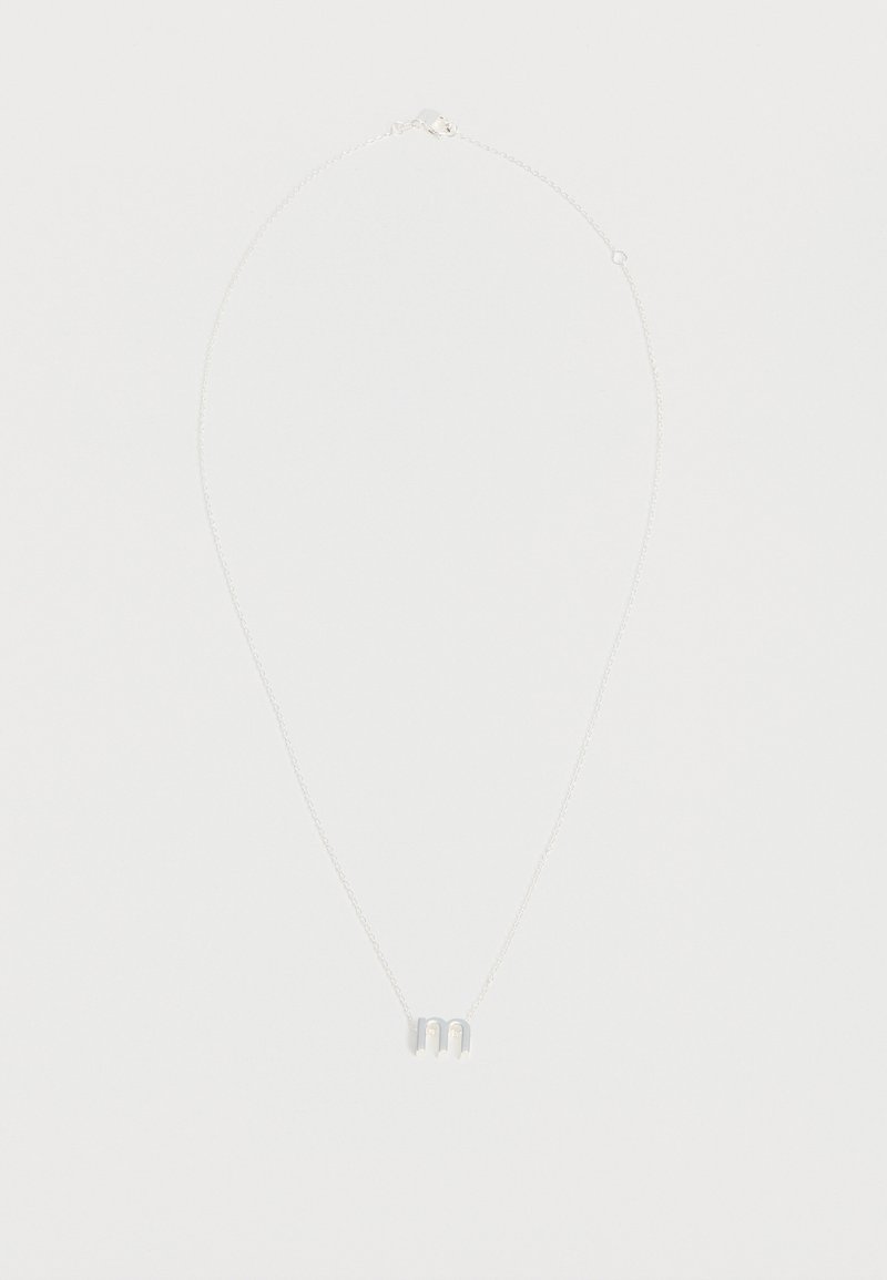 Collier délicat en chaîne argentée avec un petit pendentif en lettre minuscule "m" suspendu au centre sur un fond blanc uni.