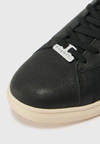 Tenis din piele neagră cu un superior texturat, șireturi negre și un detaliu proeminent cu logo argintiu. Conceput cu o talpă de culoare crem.