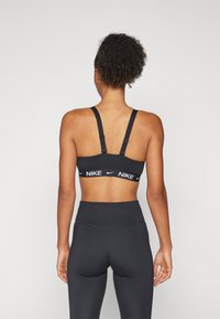 Crna sportska brusnica s podesivim trakama i bijelim Nike logom na remenu, uparena s crnim tajicama visokog struka. Glatki, rastezljivi materijal.