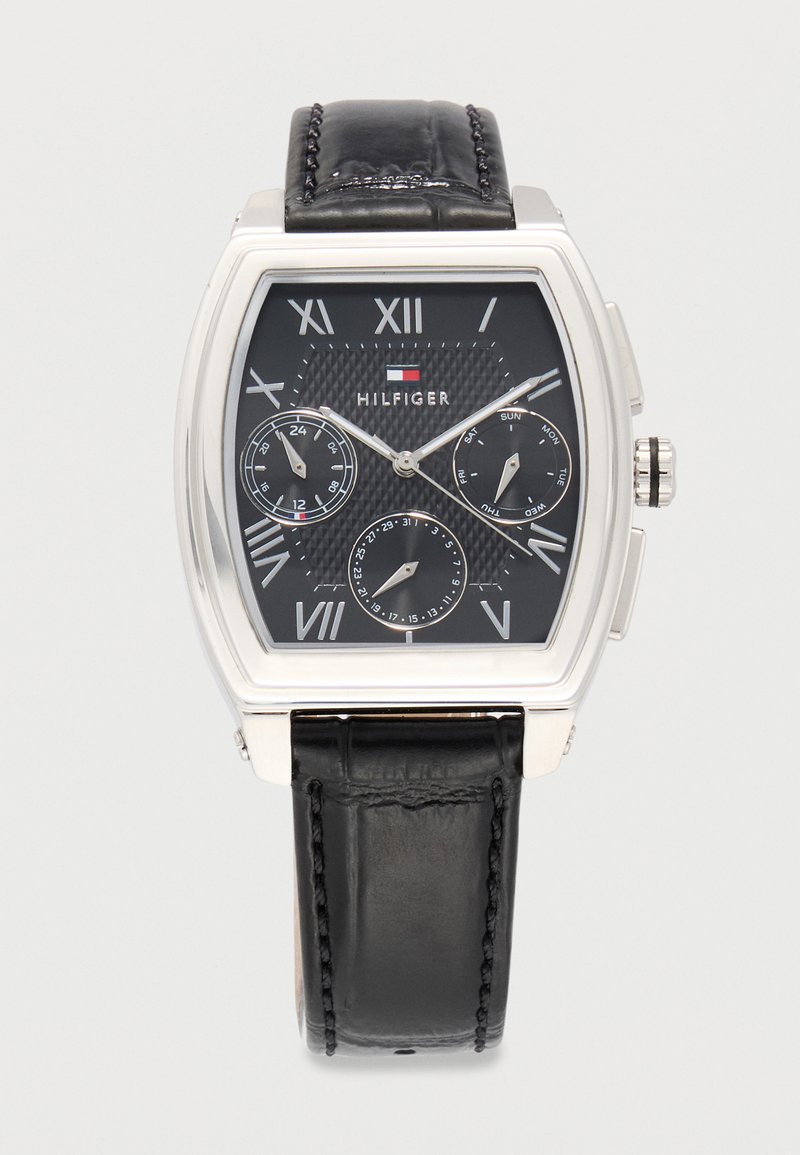 Tommy Hilfiger zapestna ura s črnim usnjenim paščkom, pravokotno srebrno ohišje, črnim številčnikom z rimskimi številkami in tremi podštevilčnicami, ki prikazujejo 24-urno uro, dan in datum.