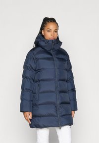 Jachetă puffer bleumarin cu guler înalt, matlasare orizontală proeminentă, buzunare laterale și închidere cu fermoar. Prezintă o textură netedă și strălucitoare.