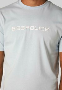 Šviesiai mėlyna trumpų rankovių marškinėlių suapvalinta apykaklė, pagaminta iš medvilnės; ant krūtinės yra iškilmingas baltas "883POLICE" logotipas.