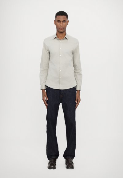 Camisa de botón de manga larga de color gris claro combinada con jeans de mezclilla azul oscuro. La camisa tiene un cuello y cierre frontal con botones.