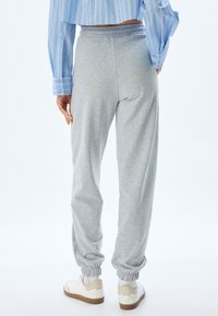 Lichtgrijze sweatpants van zacht materiaal, met een elastische tailleband en taps toelopende boorden, gecombineerd met witte sneakers.