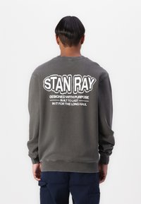 Gray sweatshirt featuring a bold white "STAN RAY" logo on the back, with additional text underneath. Regular fit and soft fabric.