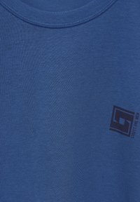 T-shirt di cotone blu con colletto a girocollo a coste. Presenta un piccolo logo stampato nero nell'angolo in basso a destra. Texture liscia.