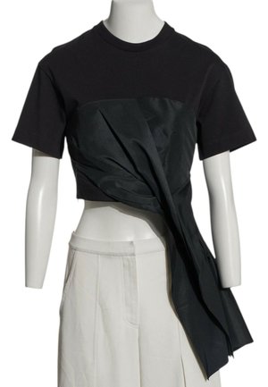 Zwarte korte mouw cropped top met vastgemaakt lang gedrapeerd stof over witte hoge taille wijde broek op paspop.