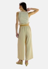 Beige mouwloze top met gerimpelde zoom, gecombineerd met luchtige, wijdlopende beige broek. Bevat een geweven riem en wedges van espadrilles.