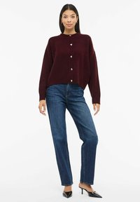 Burgunderroter Strickcardigan mit rundem Ausschnitt und silbernen, herzförmigen Knöpfen, kombiniert mit blauem Denim-Jeans mit geradem Bein und schwarzen, hochhackigen Mules.