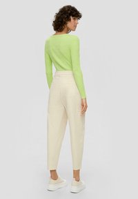 Un haut à manches longues côtelé vert citron associé à un pantalon crème fuselé et des baskets claires. La tenue présente des designs minimalistes et des textures douces.