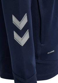 Navyblå träningströja med texturerad tyg, präglat chevronmönster i ljusgrått på ärmen och diskret logotyp.