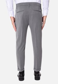 Pantaloni grigi con una texture morbida, taglio slim e due tasche posteriori, abbinati a scarpe nere e una camicia bianca.