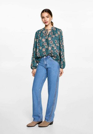 Blumenbluse in Teal mit Krawattenkragen und Ballonärmel; kombiniert mit hochgeschnittenen, hellblauen Jeans aus Denim mit Seitennähten.