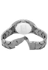 Reloj de acero inoxidable plateado con pulsera de eslabones y una caja redonda, que cuenta con un fondo transparente y una corona en el lateral.