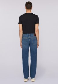 Camiseta negra de manga corta combinada con jeans rectos azules. Los jeans tienen un parche de cuero marrón en la parte trasera de la cinturilla y en los bolsillos.
