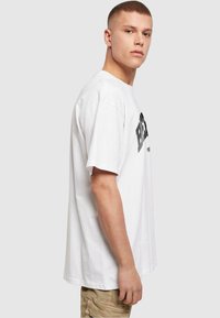Witte katoenen t-shirt met korte mouwen, voorzien van zwarte bedrukte tekst aan de voorkant. Losse pasvorm en een standaard ronde hals.