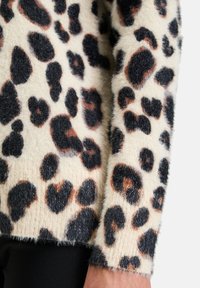 Leopardenmuster-Pullover mit einem cremefarbenen Grund und schwarzen sowie braunen Flecken, aus weichem, strukturiertem Material mit flauschigen Bündchen.