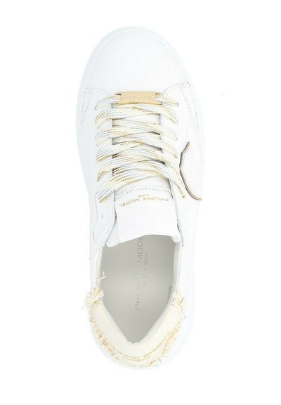 Sneaker bianco con tomaia testurizzata, dettagli dorati e lacci crema. Cuciture visibili usurate intorno alla punta e logo sulla linguetta.