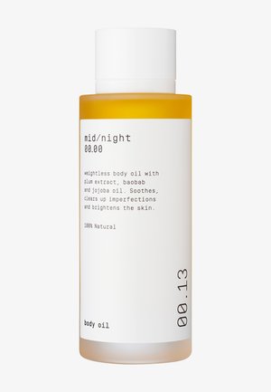 Plastic fles met een witte dop; oranje olie erin. Etiket bevat zwarte tekst op een witte achtergrond met details over ingrediënten en gebruik.