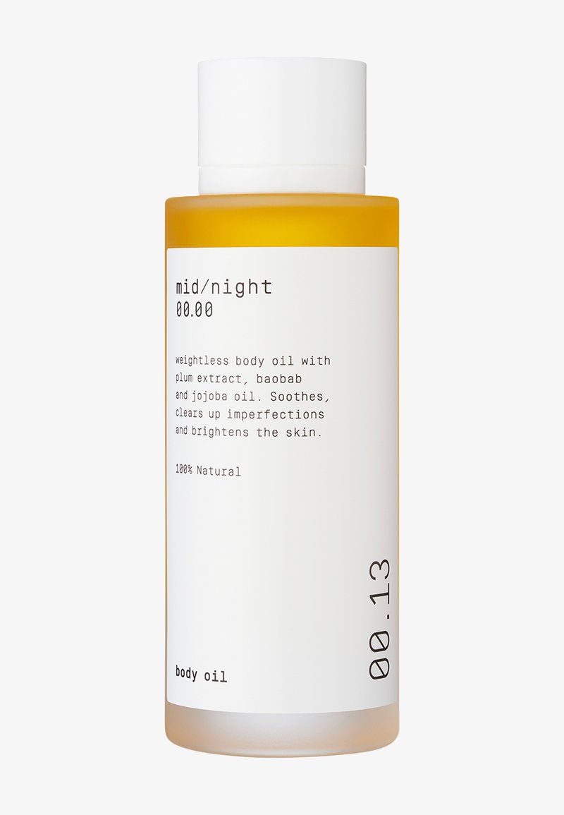 Plastflaske med hvit hette; oransje olje inni. Etiketten har svart tekst på hvit bakgrunn som beskriver ingredienser og bruk.