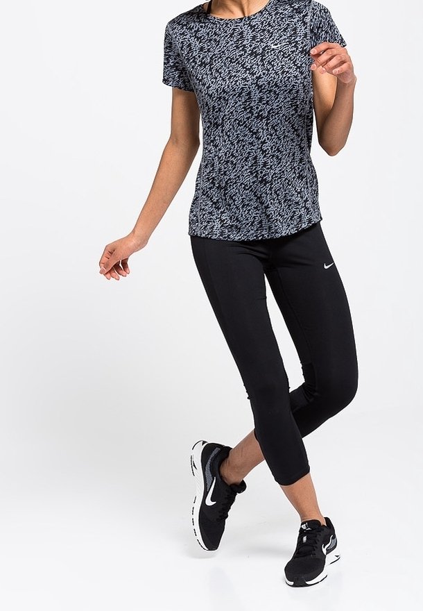 T-shirt de sport noir et blanc à motifs, associé à des leggings capri noirs. Chaussures : baskets de course noires avec des accents blancs.