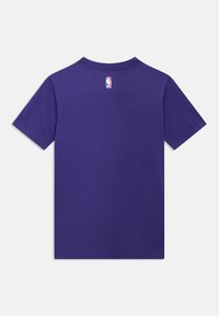 Μωβ βαμβακερό μπλουζάκι με κοντά μανίκια, στρογγυλή λαιμόκοψη και ετικέτα με το λογότυπο της NBA στο πίσω μέρος. Λείο ύφασμα και κανονική εφαρμογή.