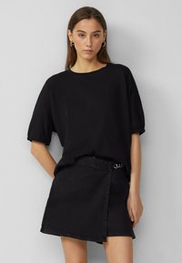 Czarna bluzka krótko rękawowa z okrągłym dekoltem i detalami przy mankietach, połączona z czarną dżinsową spódnicą o kroju kopertowym z paskiem i metalowymi akcentami.