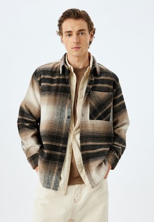 Flanellen shirt in tinten van bruin en zwart met een geruit patroon. Voorzien van een borstzak en een knoopsluiting aan de voorkant, gelaagd over een beige top.